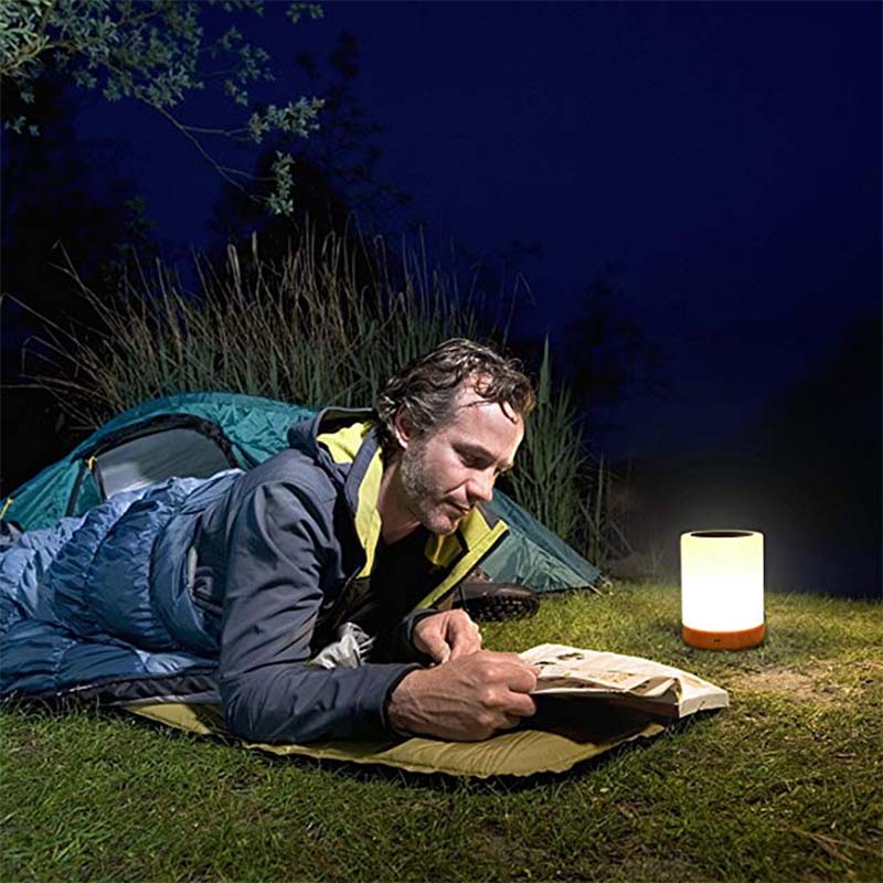 Man camping at night, reading a book next to a lantern and tent.