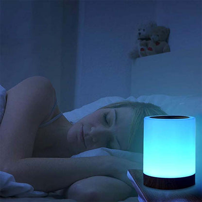 Person sleeping in bed with a colorful night light on a bedside table.