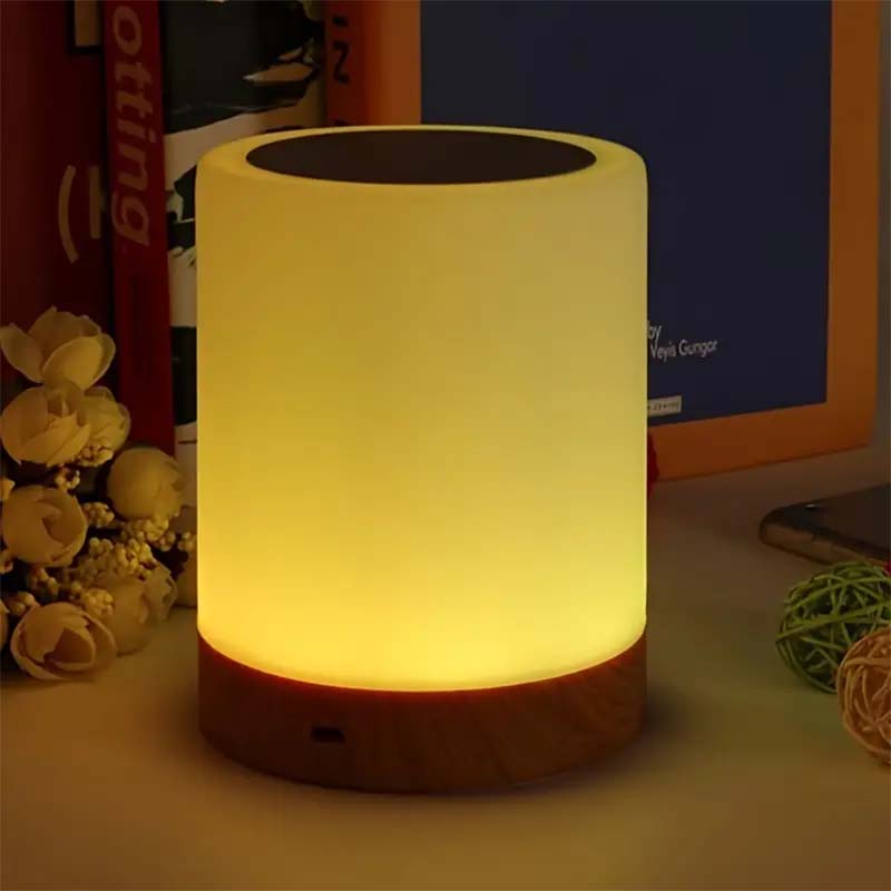 Cylindrical lamp emitting a warm glow on a surface with books and decorative items in the background.