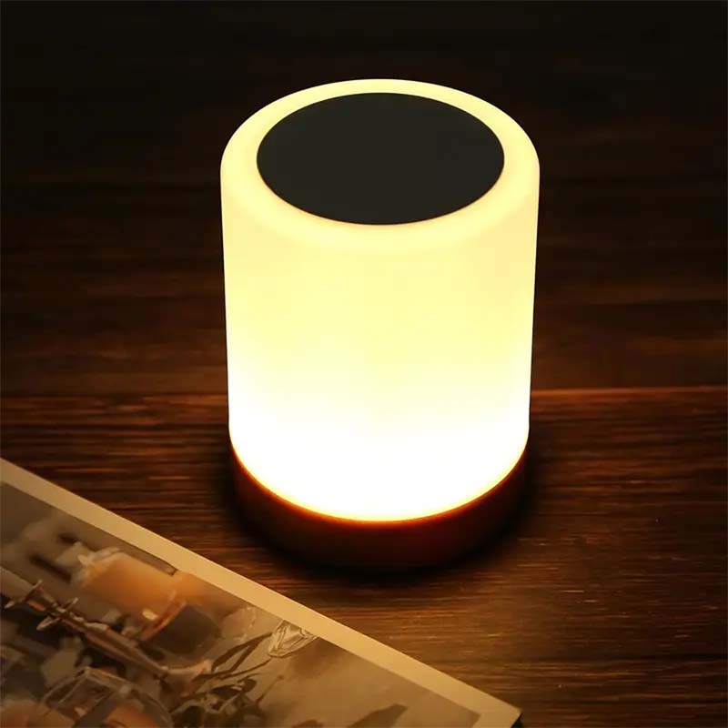 Cylindrical LED lamp emitting a warm glow on a wooden surface.
