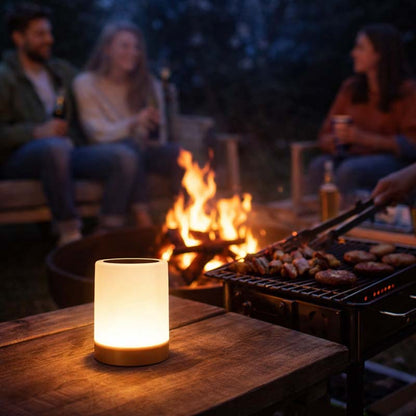 People sitting around a campfire with a lit lantern on a table in the foreground.