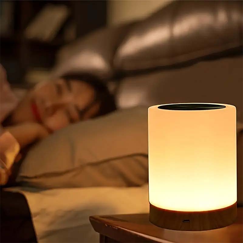 Person sleeping in bed with a night lamp on a bedside table