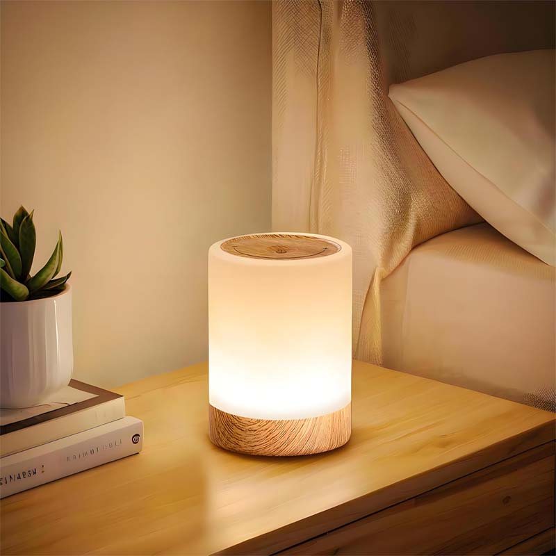 Wooden lamp on a bedside table with books and a plant in the background