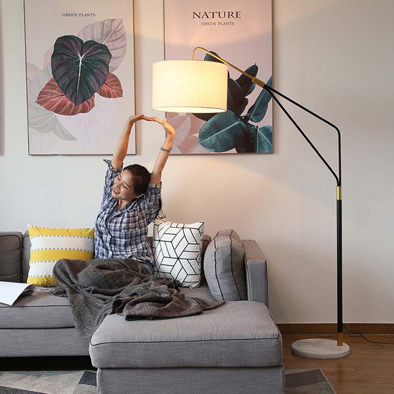 Woman with her arms raised sits on a sofa in the living room, next to a Reader Floor Lamp and a painting of leaves.