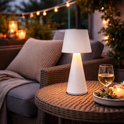 Outdoor setting with a table lamp, glass of wine, and candles on a patio.