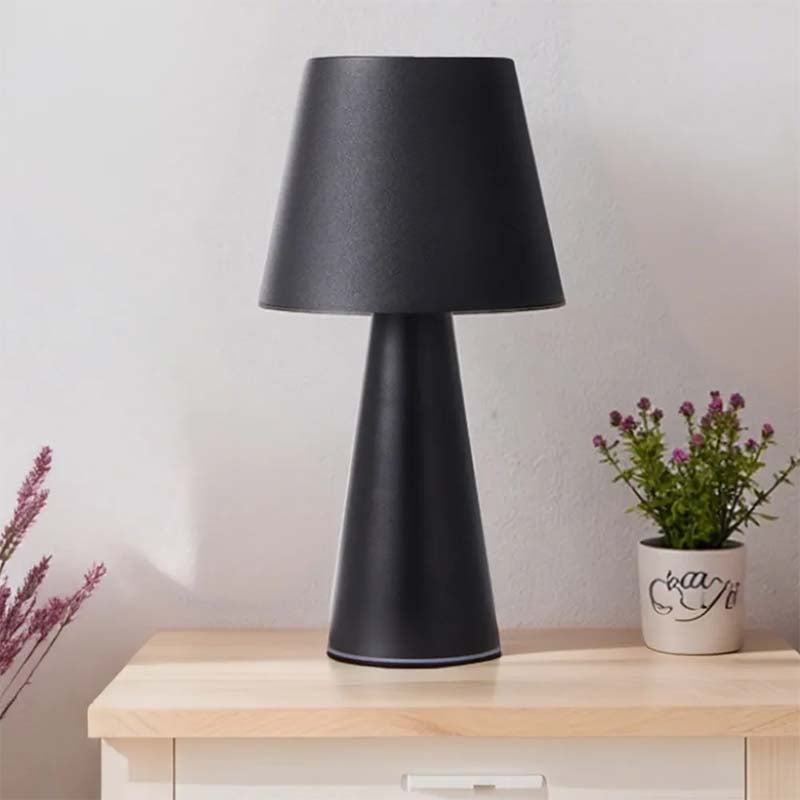 Black table lamp on a wooden surface with a plant in the background