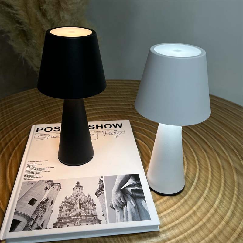 Two table lamps, one black and one white, on a magazine with a blurred background.
