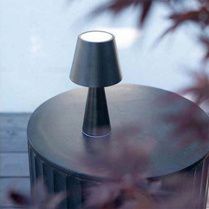 Black portable table lamp on round table outdoors with blurred background.