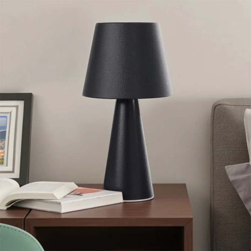 Black table lamp on a wooden side table with books and a framed picture in a room setting.