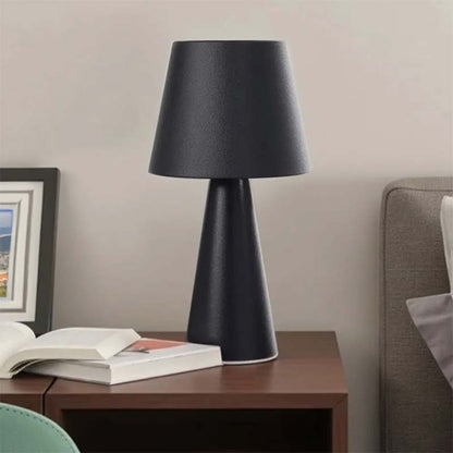 Black table lamp on a wooden side table with books and a framed picture in a room setting.