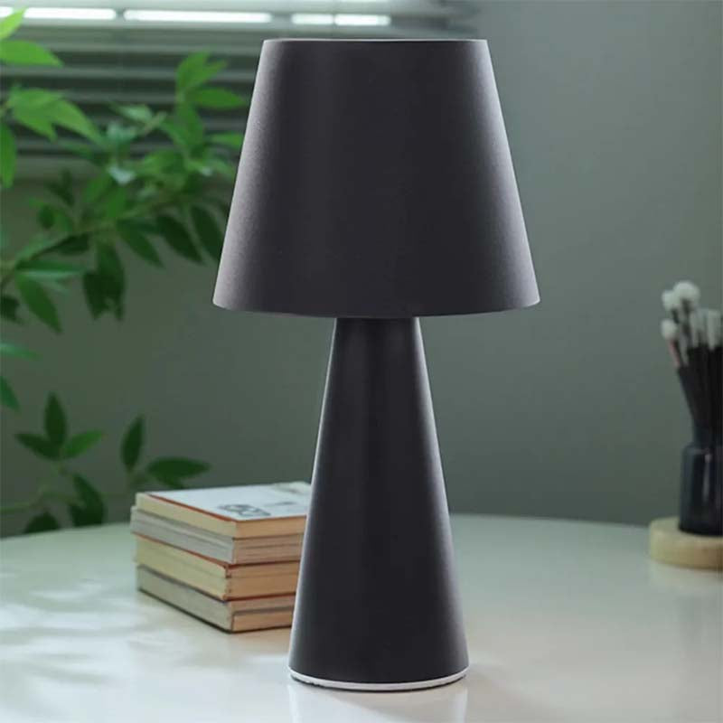 Black table lamp on a surface with books and a plant in the background
