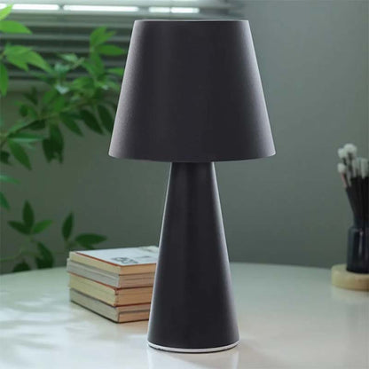 Black table lamp on a surface with books and a plant in the background