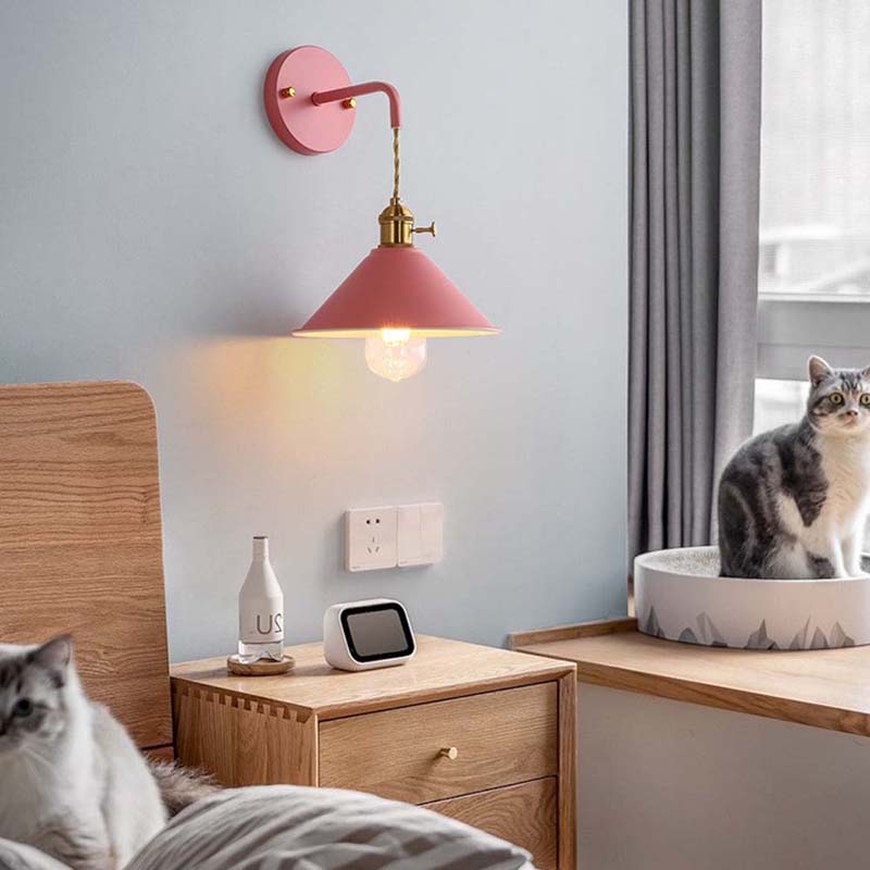 Modern bedroom with pink wall lamp, wooden nightstand, and cat sitting on a windowsill.