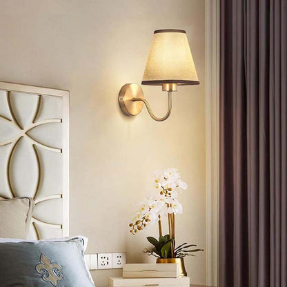 Wall-mounted lamp with a decorative headboard and plant in a bedroom setting