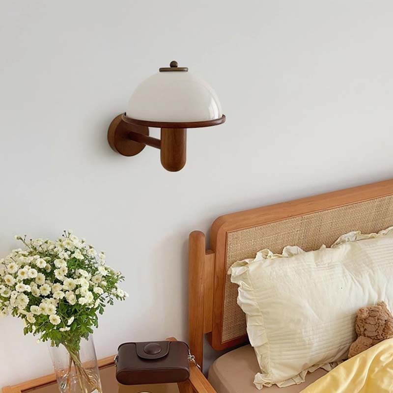 Wall-mounted lamp next to a bed with pillows and a teddy bear, on a light gray wall.