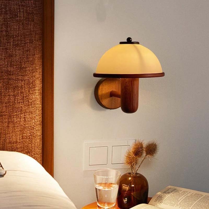Wall-mounted lamp with wooden base and yellow shade on a wall next to a bed.