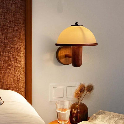 Wall-mounted lamp with wooden base and yellow shade on a wall next to a bed.