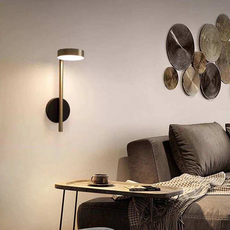 Modern wall lamp next to a sofa with decorative wall art in a living room setting.
