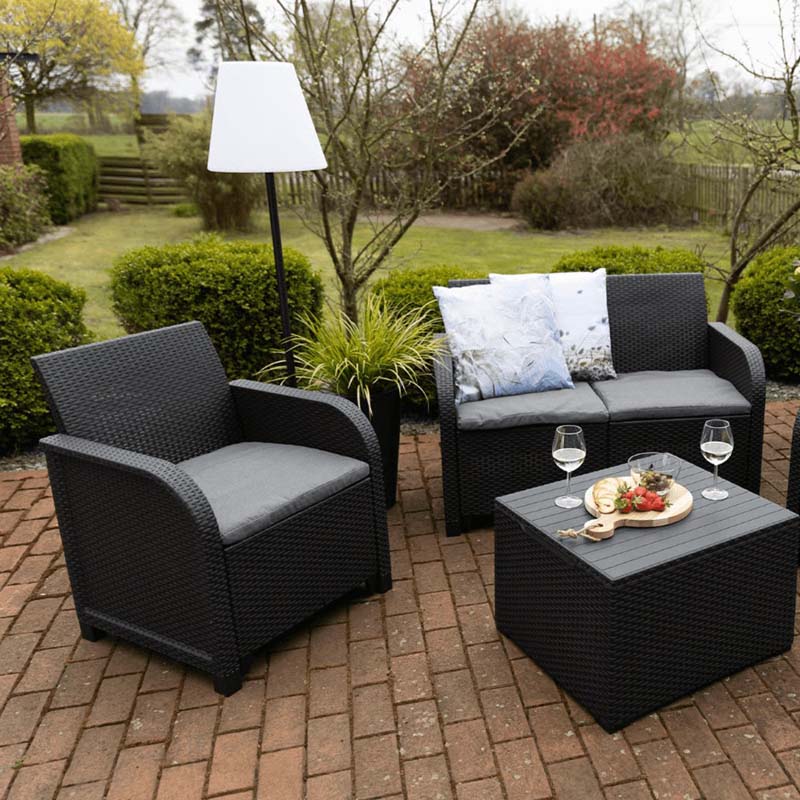 Solar RGB Floor Lamp in a patio furniture set: chairs, table and cushions on a brick deck.