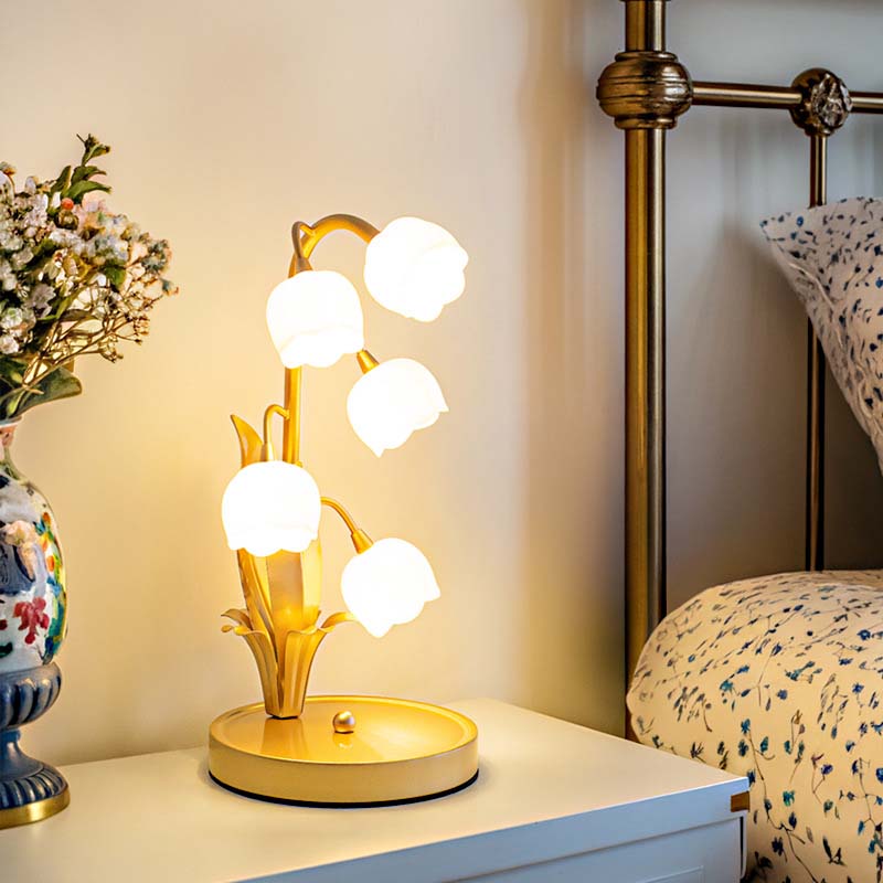 Decorative table lamp with multiple light bulbs on a bedside table next to a vase with flowers and a bed.