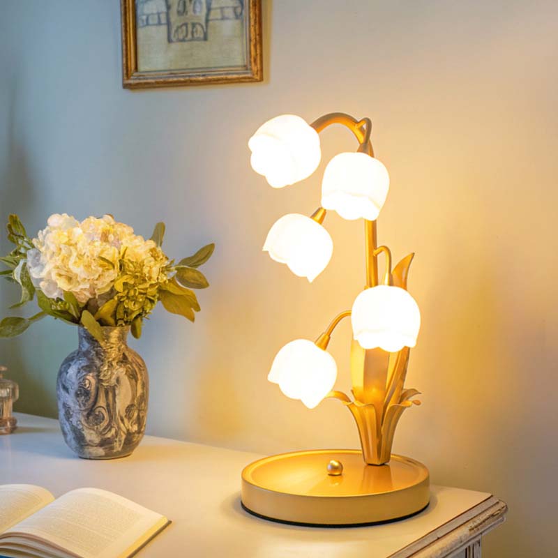 Decorative table lamp with floral design on a nightstand next to a vase of flowers and an open book.
