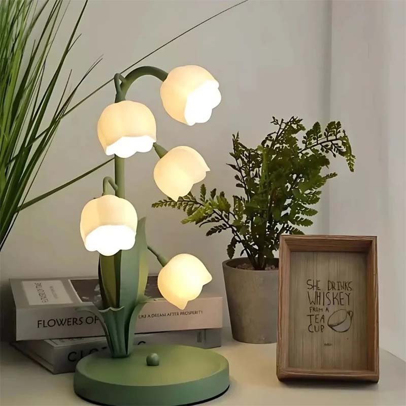Decorative lamp with flower-shaped lights on a surface with plants and books in the background.