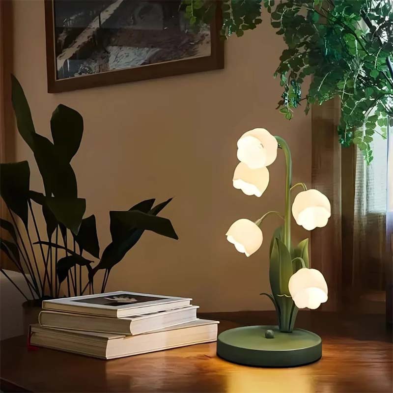 Decorative table lamp with floral design on a wooden surface, surrounded by books and plants.