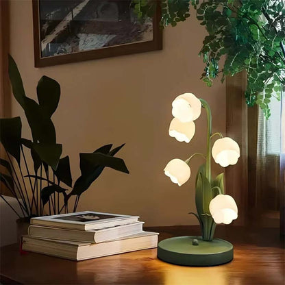 Decorative table lamp with floral design on a wooden surface, surrounded by books and plants.