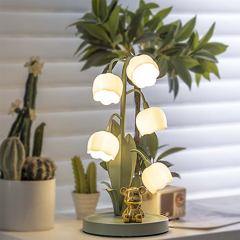 Decorative table lamp with a teddy bear base, surrounded by potted plants on a light-colored surface.