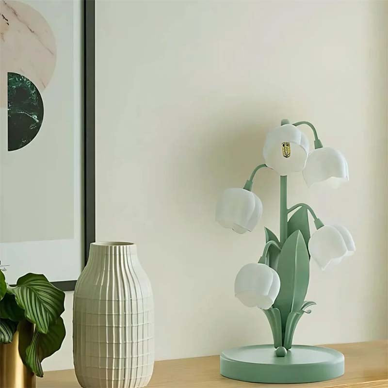 Decorative lamp with floral design on a table next to a white vase and plant.