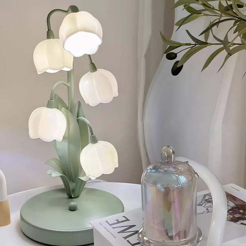 Decorative table lamp with tulip design on a surface with a plant in the background