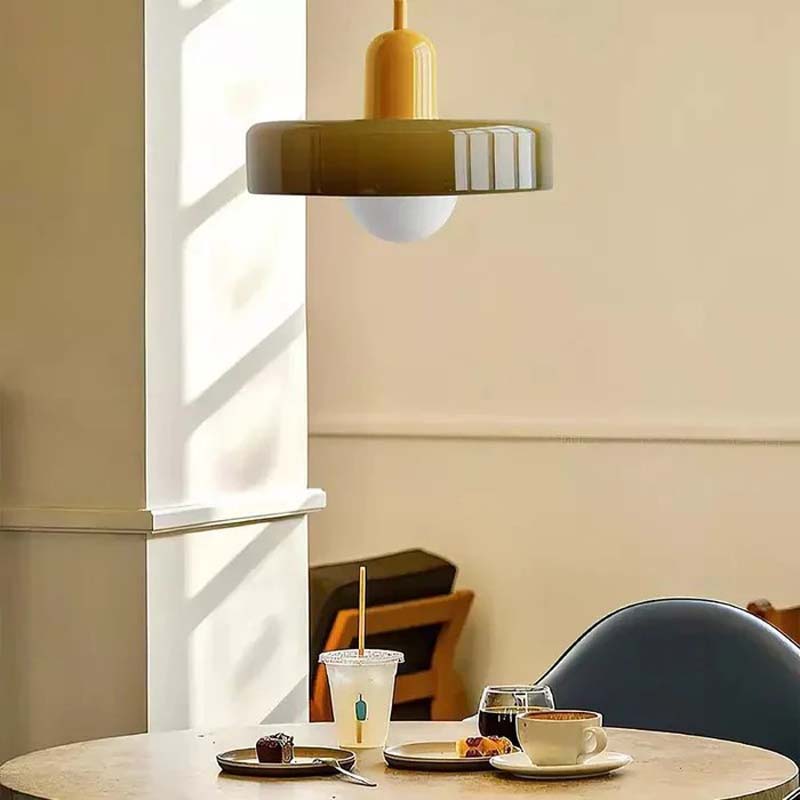 The Color Glow Pendant Light hangs above a dining table with a cup and saucer, a glass, and a dessert.