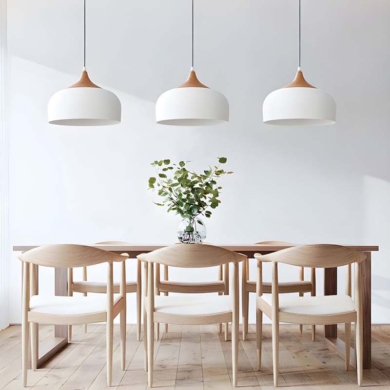 Dining area with wooden table and chairs under three pendant lights in a minimalistic setting.