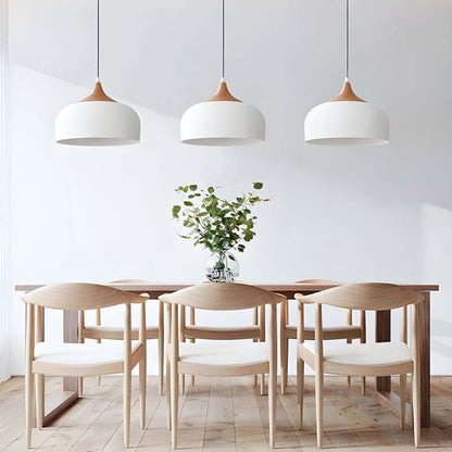 Dining area with wooden table and chairs under three pendant lights in a minimalistic setting.