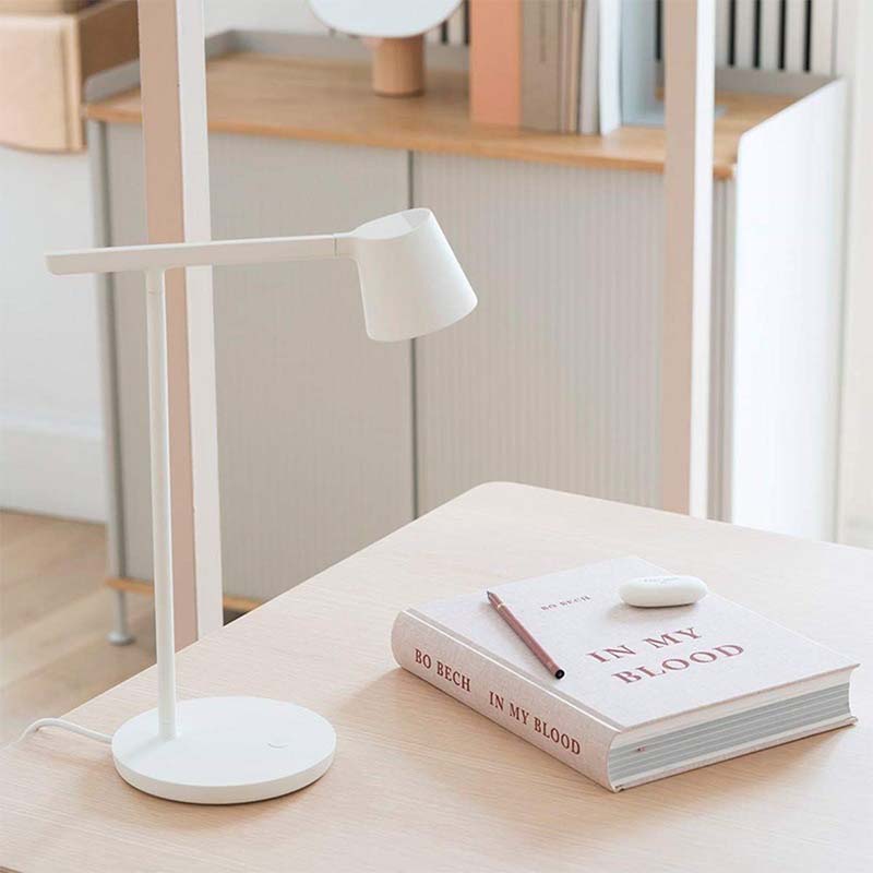 White desk lamp on a wooden surface with a book and pen in the background