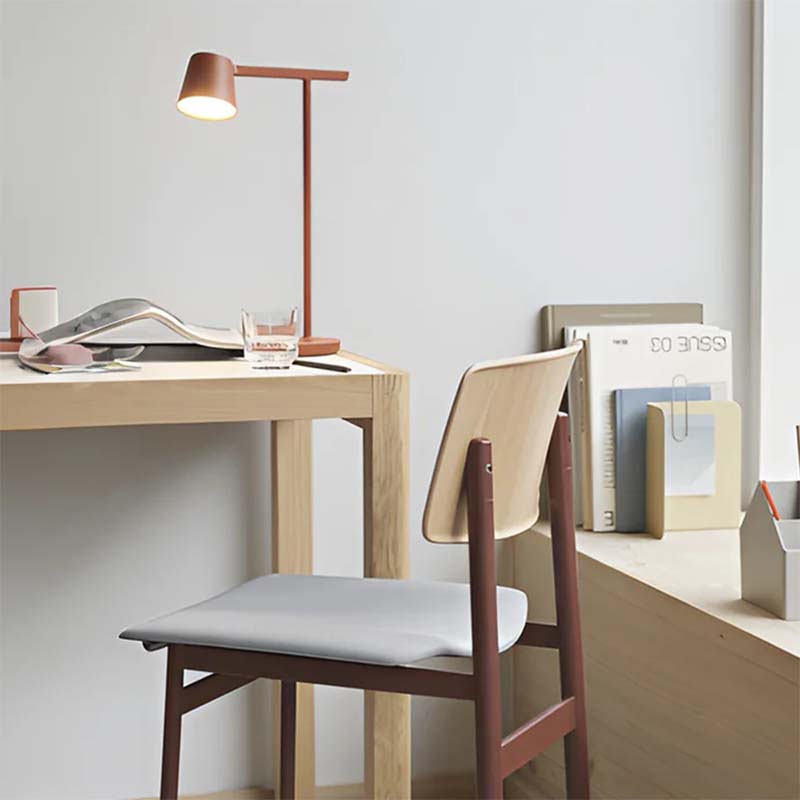Minimalist desk setup with a chair, lamp, and books in a room.