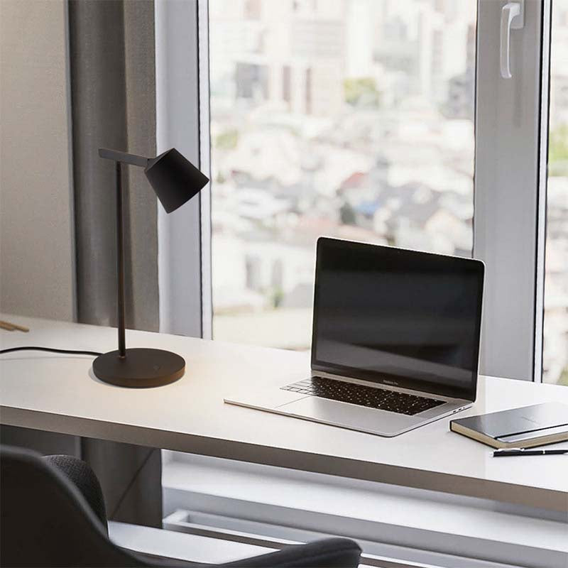 Modern office desk with laptop, lamp, and notebook by a window
