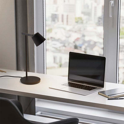 Modern office desk with laptop, lamp, and notebook by a window