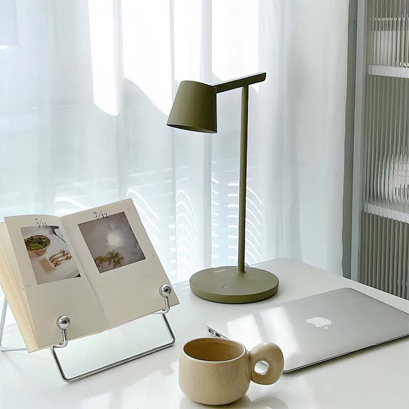 Desk setup with a lamp, laptop, photo frame, and mug in a bright room.