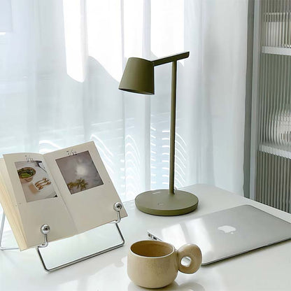 Desk setup with a lamp, laptop, photo frame, and mug in a bright room.