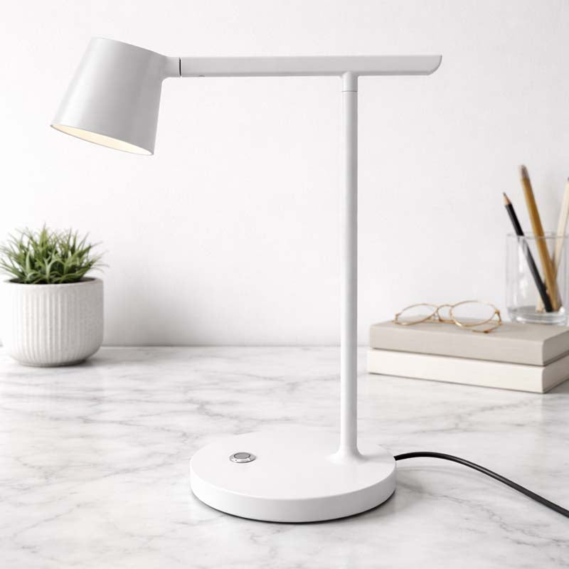White desk lamp on a marble surface with books, glasses, and a plant in the background.