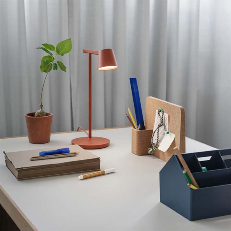 Desk setup with a lamp, notebook, pen, plant, and office supplies against a neutral background