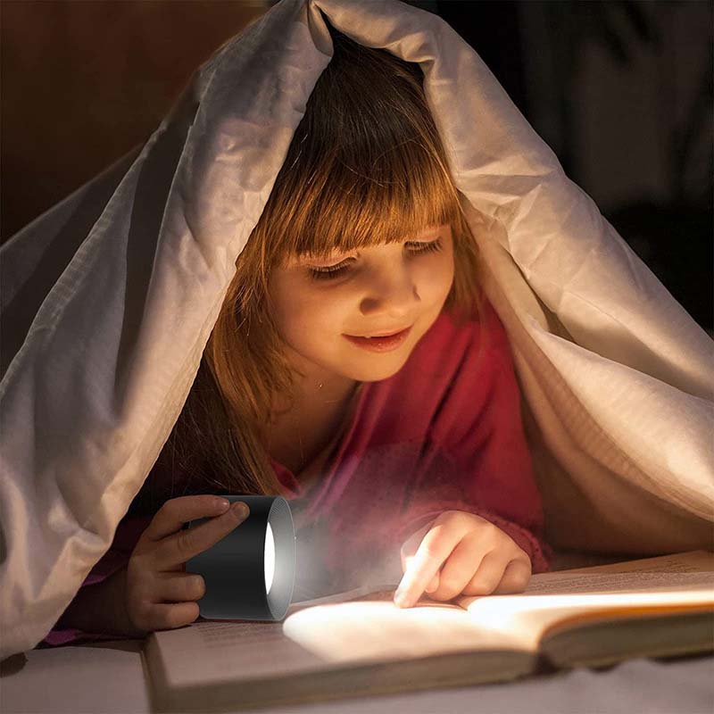 Child reading a book under a blanket with a flashlight