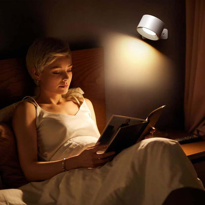 Woman reading a book in bed under a wall-mounted lamp