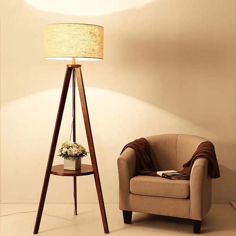 Triangular wooden floor lamp with a beige lampshade next to a beige armchair in a softly lit room.