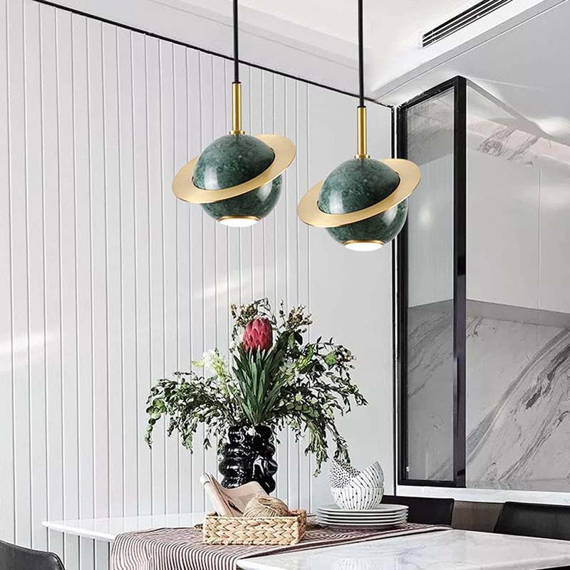 Modern interior design with green and gold pendant lights, a vase of flowers, and a marble countertop.
