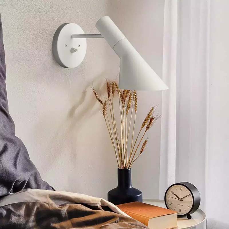 White wall lamp on a neutral wall with a vase of dried plants and a clock on a nightstand.