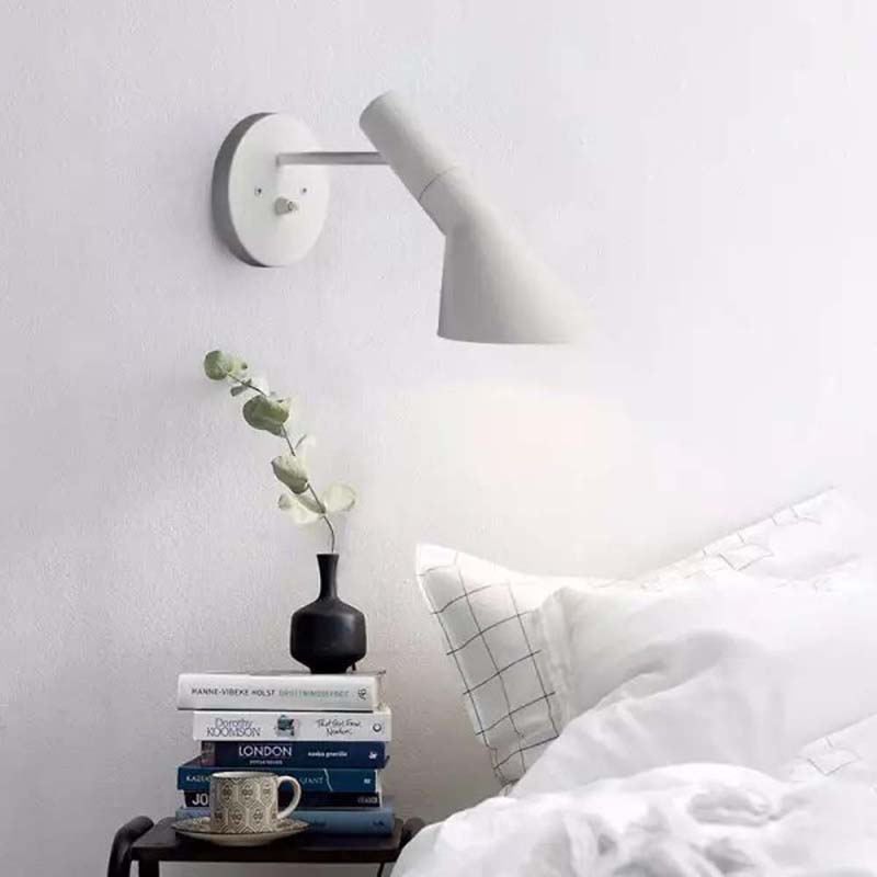 White wall lamp above a stack of books with a cup and plant on a bedside table.