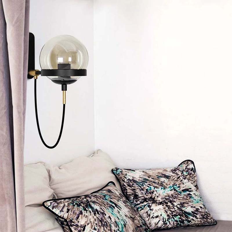 Decorative wall lamp with a glass shade on a white wall above a bed with patterned pillows.