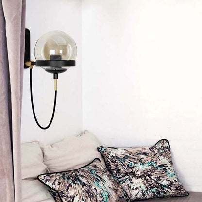 Decorative wall lamp with a glass shade on a white wall above a bed with patterned pillows.